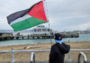 A Canadian boy tourist holds a Palestinian flag aloft signalling to "no war" protesters on Devonport wharf