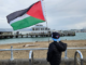A Canadian boy tourist holds a Palestinian flag aloft signalling to "no war" protesters on Devonport wharf