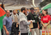 Olivia Coote presents a welcome home koha to Global Sumud Flotilla activists Mousa Taher (centre) and Hāhona Ormsby (black cap) at Auckland International Airport