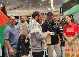 Olivia Coote presents a welcome home koha to Global Sumud Flotilla activists Mousa Taher (centre) and Hāhona Ormsby (black cap) at Auckland International Airport