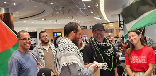Olivia Coote presents a welcome home koha to Global Sumud Flotilla activists Mousa Taher (centre) and Hāhona Ormsby (black cap) at Auckland International Airport