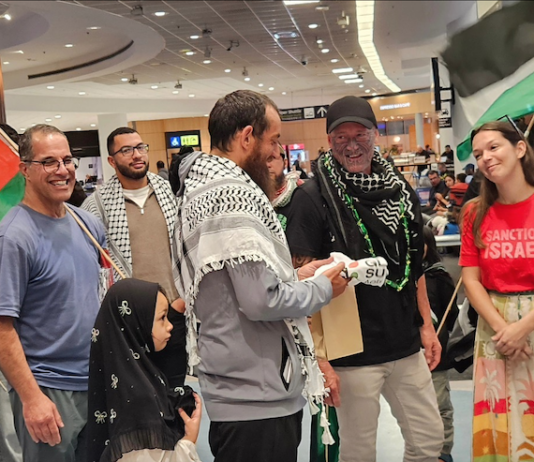 Olivia Coote presents a welcome home koha to Global Sumud Flotilla activists Mousa Taher (centre) and Hāhona Ormsby (black cap) at Auckland International Airport