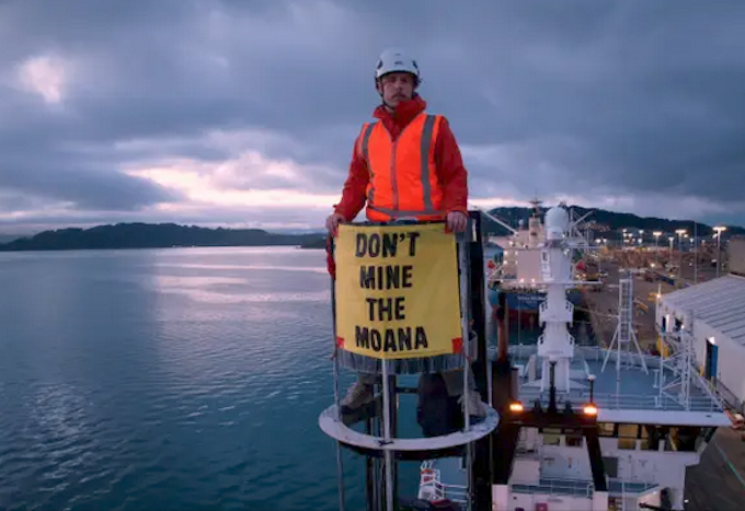 A Greenpeace protester on board the Tangaroa holds a banner saying "Don't Mine the Moana"